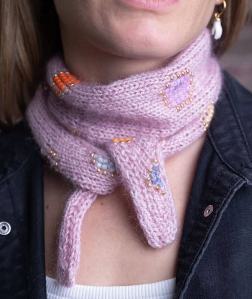 Person wearing a pink knitted scarf with decorative beads, close-up shot.