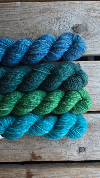 four skeins on wood background. one in teal, one in green, one in dark teal one in blue