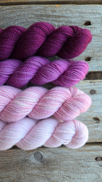 four skeins on wooden background one in light pink, one in pink, one in light purple, one in dark purple