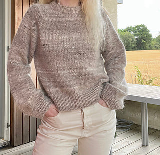 Person wearing a knitted sweater and light-colored pants on a wooden deck with a natural background