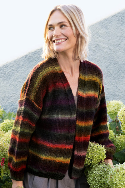 Woman wearing a colorful striped sweater standing outdoors with mountains in the background