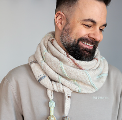 A person wearing a striped knitted wrap with multi colored strands, smiling.