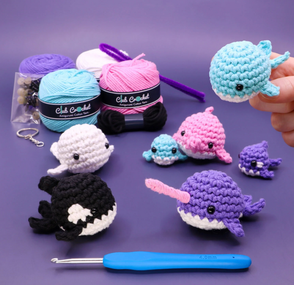 Collection of colorful crochet sea creature toys with yarn balls and a crochet hook on a purple background.