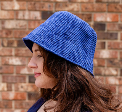 Person wearing a blue crochet hat against a brick wall