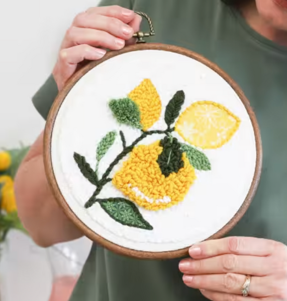 a woman holding an embroidery hoop with   a punch needle project in the hoop