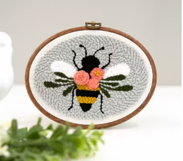 An embroidery hoop with a punch needle project of a bee with a grey background