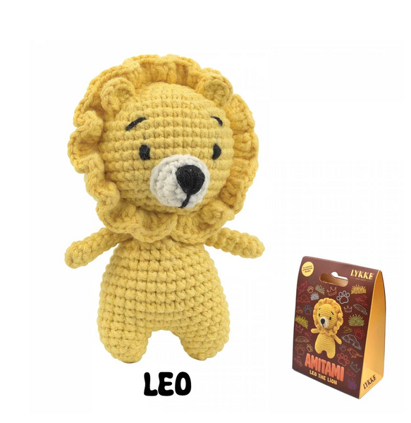 A yellow crocheted lion amigurumi toy with a white snout and black embroidered eyes and nose, shown next to its retail packaging box. The text 'LEO' is written below the toy.
