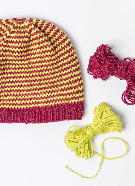 Knitted hat with pink and yellow stripes and two balls of yarn on a white background