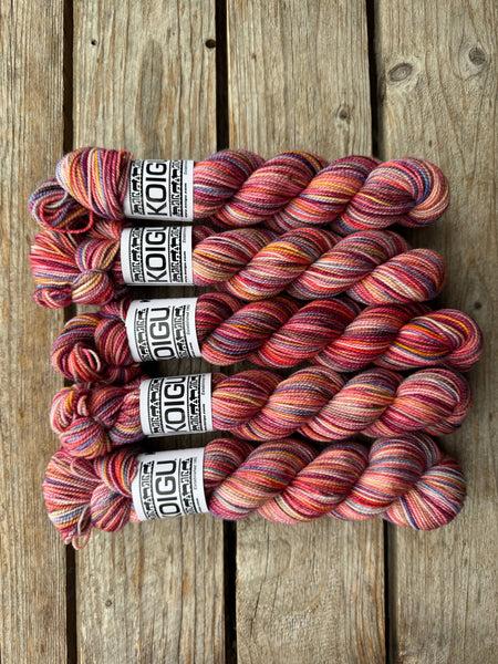 five skeins of yarn on wooden board in colors of red, purple, orange, and dark red