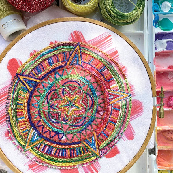 Colorful embroidered mandala in an embroidery hoop with thread spools in the background.
