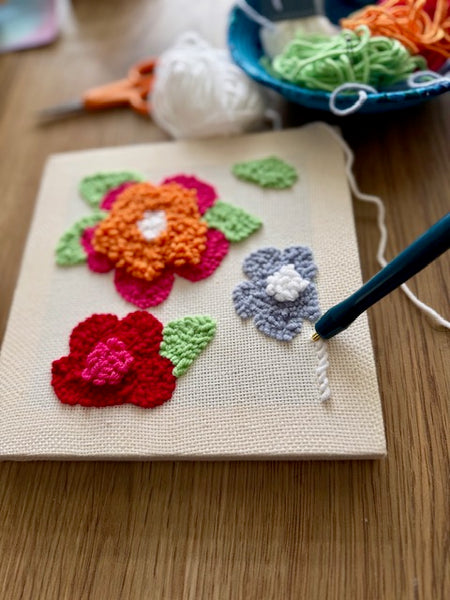 yarn flowers on a canvas with yarn and scissors in the background