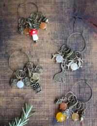 A collection of stitch markers made with semi-precious gemstones, Czech glass beads, and antiqued bronze charms, displayed on a wooden surface.

Owl & Hare