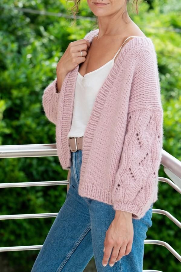 Woman wearing a light pink cardigan with cable sleeves made with Laines du Nord Firenze yarn.